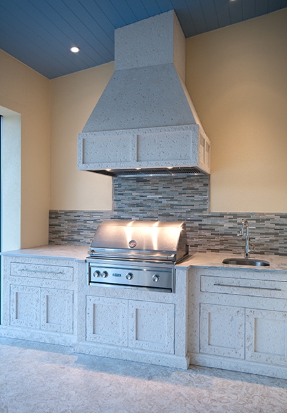 Outdoor Kitchen with a grill in sink in custom stone cabinets and hood with a stone back splash